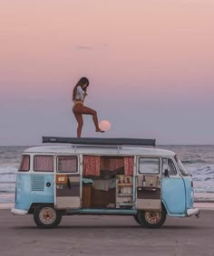 a woman standing on top of an old van at the beach