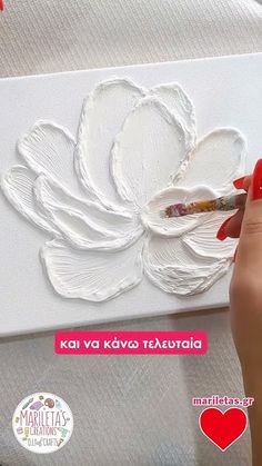 a woman is painting a flower with white paint on the canvas and red nail polish