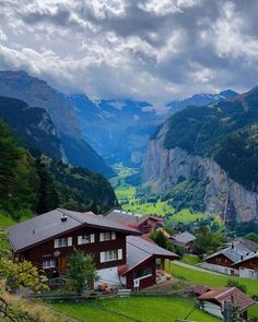 the mountains are covered with green grass and houses in the foreground, under a cloudy sky