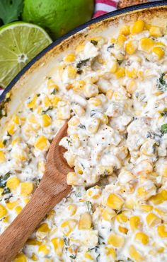 a skillet filled with corn and cheese next to limes