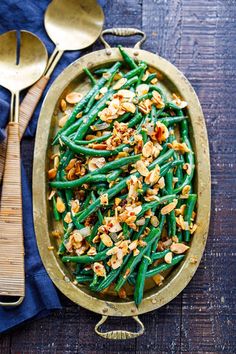 green beans and walnuts in a gold serving dish with two spoons on the side