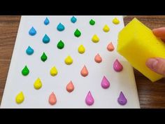 a person is using a sponge to paint drops on a paper board with yellow and pink colors