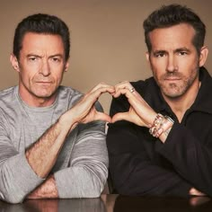 two men sitting at a table with their hands in the shape of a heart