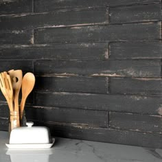 wooden utensils are sitting on a white stand in front of a black brick wall