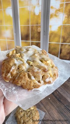 a person holding up a cookie with icing on it in front of a window