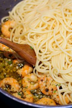 pasta with shrimp and pesto being stirred in a skillet by a wooden spoon