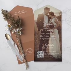 an orange wedding card with a photo on it next to a feather and flower bouquet