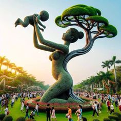 a large sculpture in the shape of a woman holding a baby on her arm with people walking around it