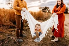 a man and woman holding a baby in a hammock while standing next to each other