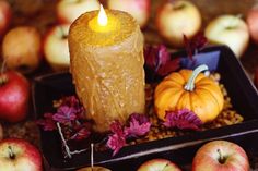 a candle sitting on top of a tray filled with apples and other fall decorations in front of them