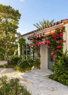 a white house with pink flowers growing on it's roof and side walk leading to the front door