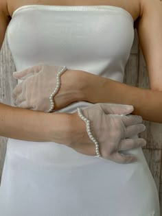 a woman wearing white gloves with pearls on her wrist