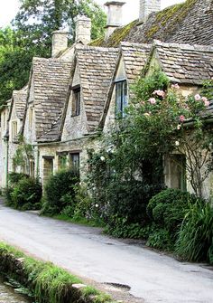 an old stone house with ivy growing on the roof and windows next to a river