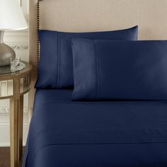 a bed with blue sheets and pillows on top of it next to a night stand