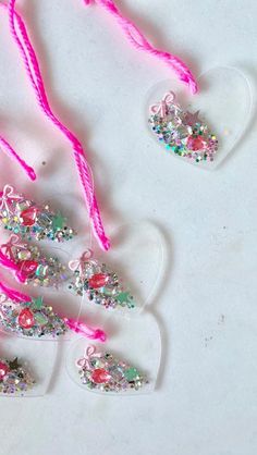 three heart shaped ornaments with pink string on white table top next to each other and one hanging ornament in the shape of a tree