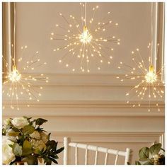 three lights hanging from the ceiling above a table with flowers and vases on it