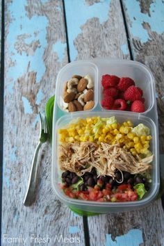 a plastic container filled with salad, fruit and veggies next to nuts on top of a wooden table