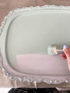 a woman is painting a large tray with white paint and a brush in her hand