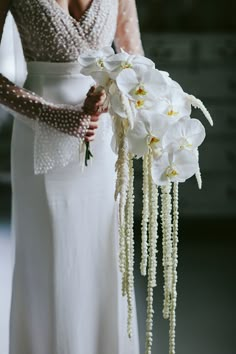 a woman in a white dress holding a bouquet of flowers with pearls on the side