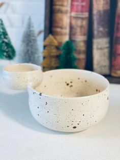 two white bowls sitting on top of a counter next to bookshelves and christmas trees