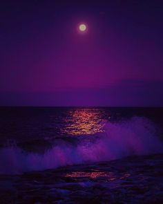 the moon is setting over the ocean with purple hues and waves crashing in front of it