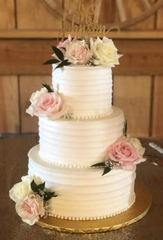 a three tiered white cake with pink and white flowers on the side, sitting on a gold platter