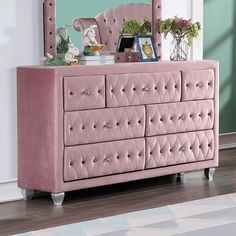 a pink dresser with a mirror on top and flowers in the vases next to it