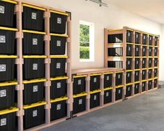 there are many black bins in the room with yellow shelves on each side and windows above them