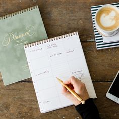 a person writing on a notepad next to a cup of coffee