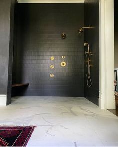 a bathroom with black tile and gold fixtures on the wall, along with a rug