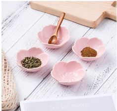 four pink bowls filled with different types of spices on top of a white wooden table