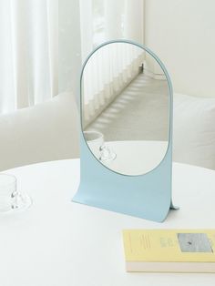 a mirror sitting on top of a white table next to a book and glass cup