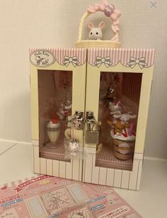 a small doll house with two glass doors and pink accessories on the front, one door open