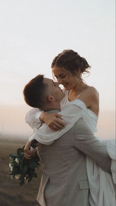 a bride and groom embracing each other in the field