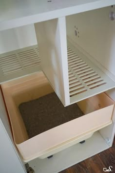 the bottom shelf of a white cabinet with a cat litter box in it's drawer