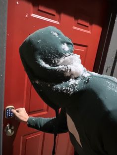 a person in a batman costume opening a red door with snow on the top and bottom