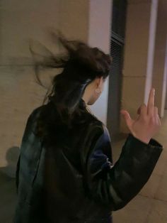 a woman with her hair blowing in the wind while standing on a sidewalk next to a building