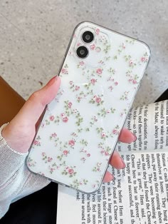 a woman is holding up her phone case in front of an open book with flowers on it