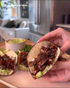 a person is holding up two tacos with meat and avocado