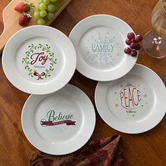 four white plates on a table with fruit and wine glasses next to them, including grapes