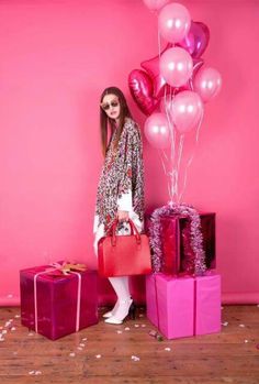 a woman standing next to pink presents and balloons