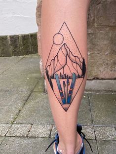 a person's legs with skis and mountains tattoo on their leg, while they are standing in front of a brick wall