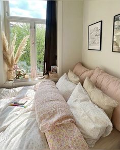 an unmade bed with many pillows and blankets on it in front of a window