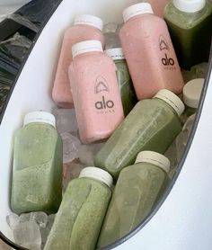 several bottles and containers filled with green smoothies on top of some ice cubes