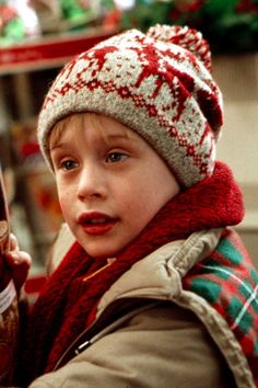 a young boy wearing a red and white knitted hat holding a cell phone in his hand