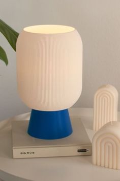 a white and blue lamp sitting on top of a table next to a book with a plant in it