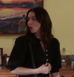 a woman standing in front of a dresser holding a black purse and looking off to the side