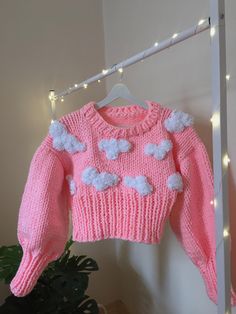 a pink sweater with white pom - poms hanging on a clothes rack