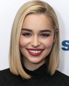 a close up of a person with blonde hair and a smile on her face, wearing a black top