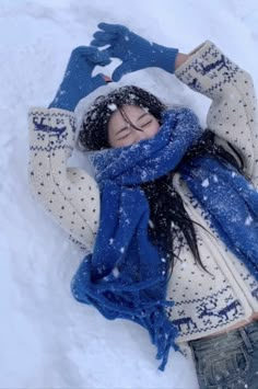 a woman laying in the snow with her hands up to her head and wearing a blue scarf